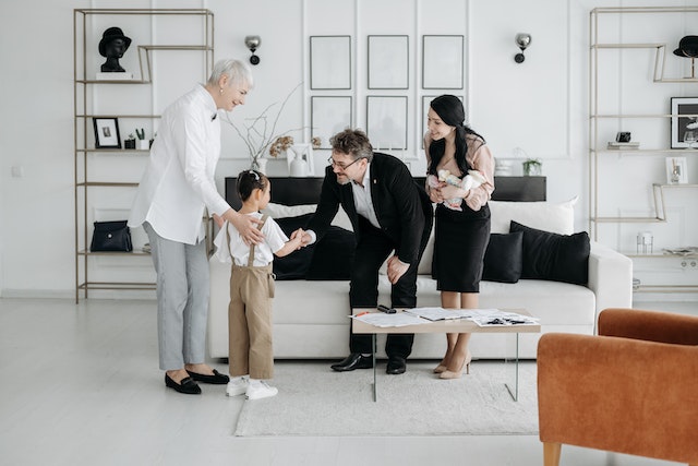 Four people in a living room, one adult is shaking a child's hand